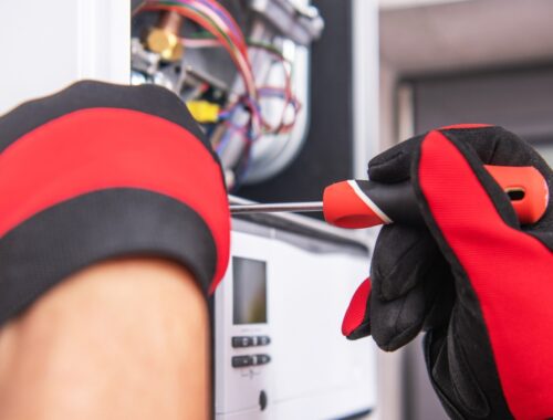 Gas Testing & Gas Purging Services | Commercial Gas Pipework Gas engineer wearing protective gloves working on a commercial boiler control unit with a screwdriver