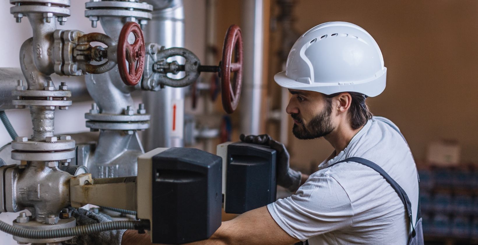 Commercial gas engineer in a white hard hat adjusting valve actuators on plant room pipework